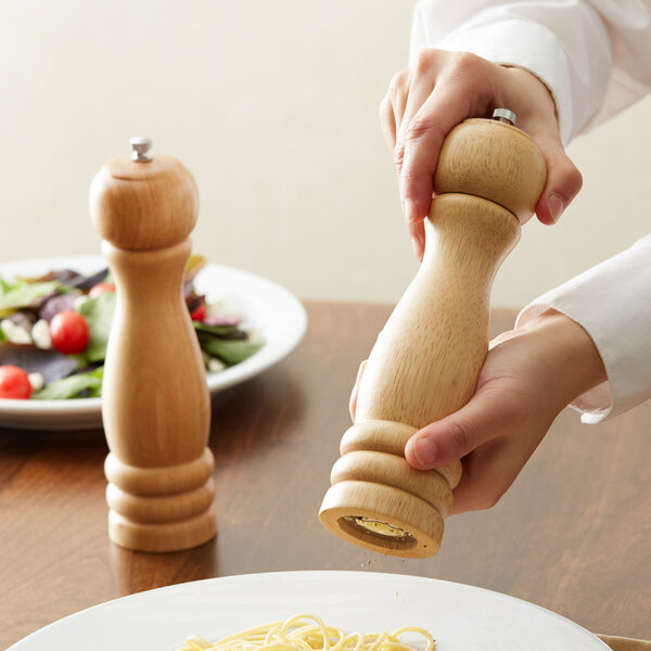A person using an Acopa wooden pepper mill on a plate.