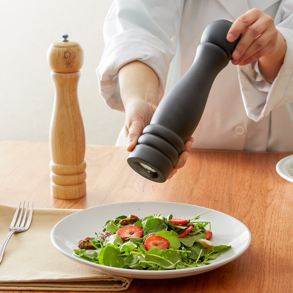 A person grinding pepper from an Acopa wooden pepper mill onto a salad.