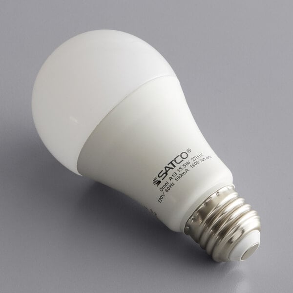A Satco frosted warm white LED light bulb on a gray surface.