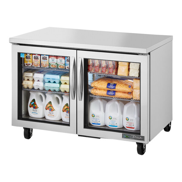 A True undercounter refrigerator with glass doors filled with white plastic containers with a logo on them.