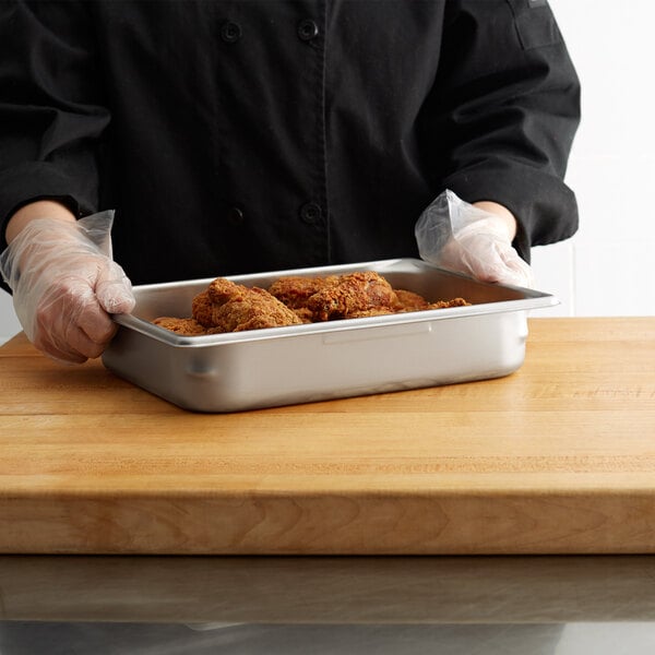 A person in a chef's uniform holding a Vollrath stainless steel hotel pan of food.