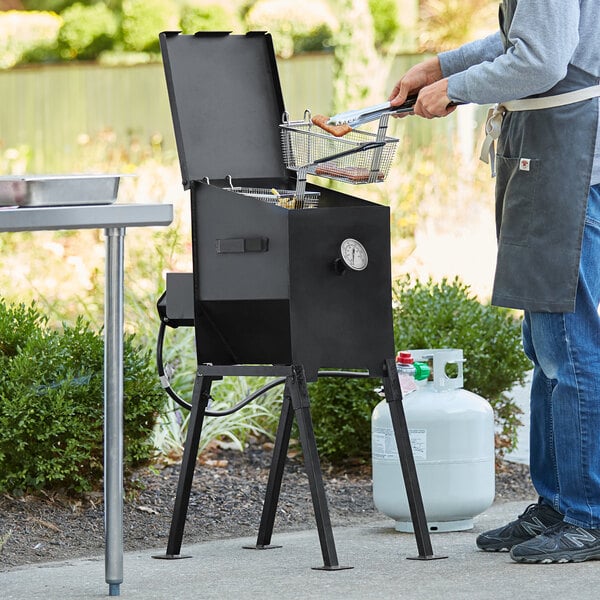 A man using a Backyard Pro 4 gallon liquid propane deep fryer to cook food on a table outdoors.