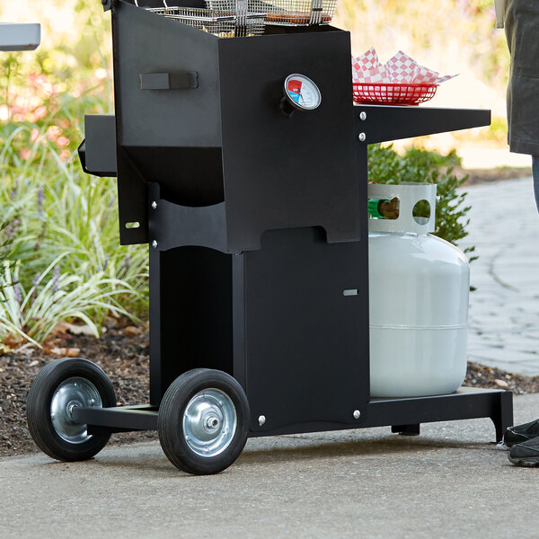 A man standing next to a black barbecue grill with a white gas cylinder.