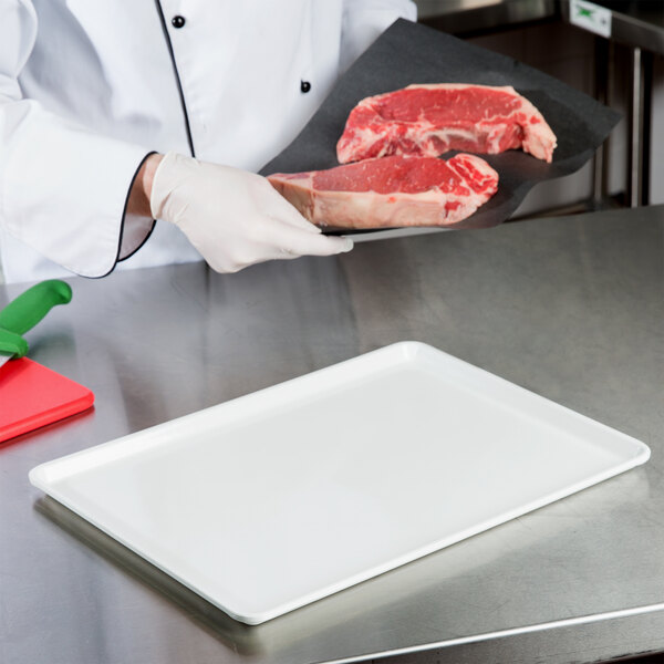 A chef holding a white rectangular tray with meat on it.
