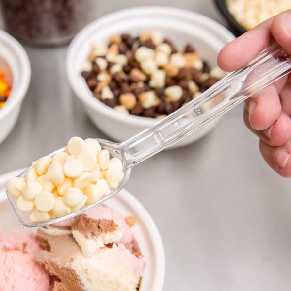 A person holding a Carlisle clear salad bar spoon full of white food over a bowl.