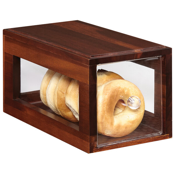 A bagel in a walnut square bread box on a bakery display table.