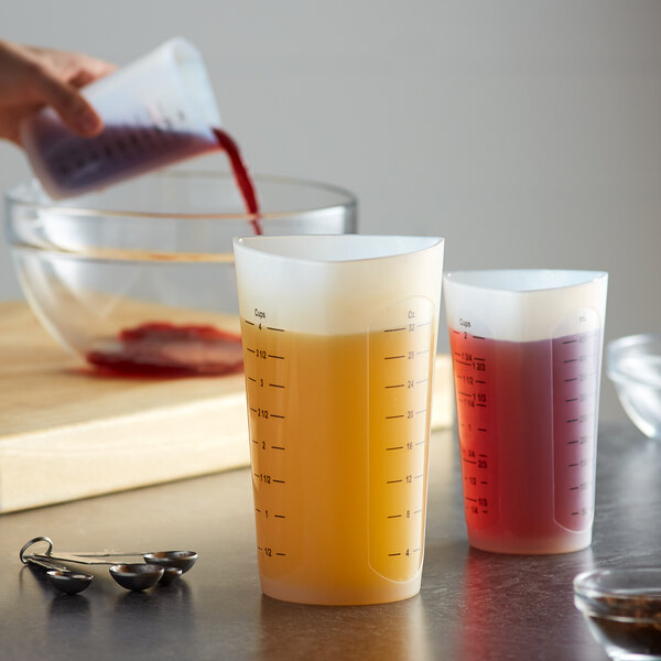 A woman using a Tablecraft flexible silicone measuring cup to pour orange liquid into a bowl.