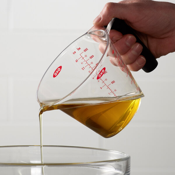 A hand pouring liquid into a bowl using an OXO clear plastic measuring cup.