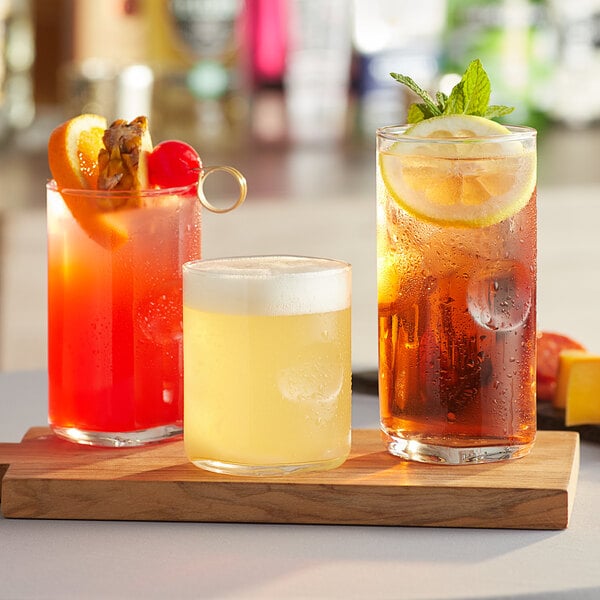 A set of Acopa thumbprint rocks glasses with three drinks on a wooden tray.
