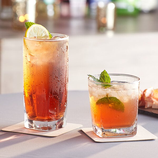 Two Acopa Cube Rocks glasses filled with iced tea on coasters with mint and lemon slices.