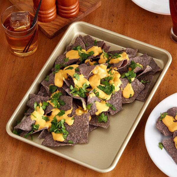 A Baker's Mark gold non-stick aluminum sheet pan of nachos with cheese sauce on a table.