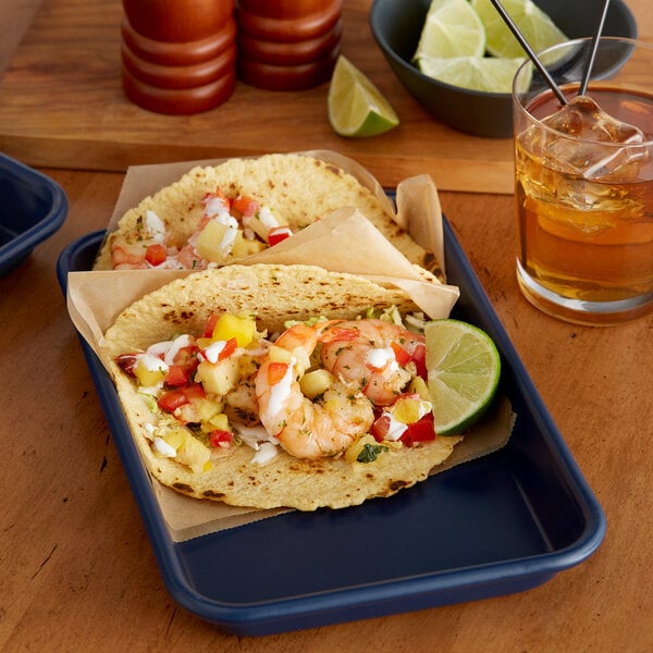 A plate of shrimp tacos on a Baker's Mark dark blue tray with a glass of liquid.