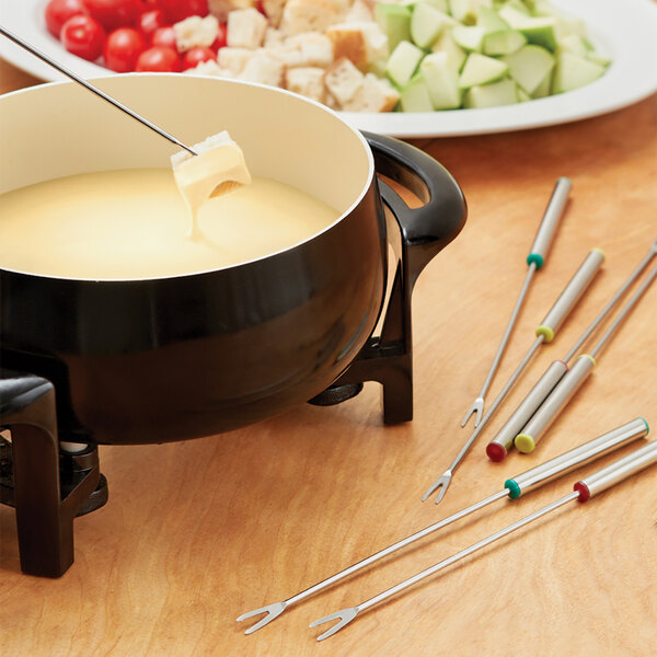 A Fox Run fondue pot with several stainless steel fondue forks with color coded handles on a table.