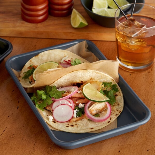 A Baker's Mark aluminum tray with two tacos and a glass of brown liquid with ice on a table.