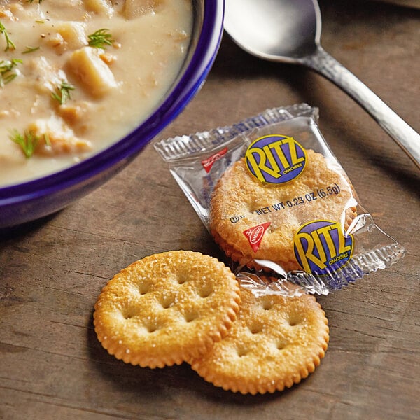 A bowl of soup with a cracker next to a spoon.