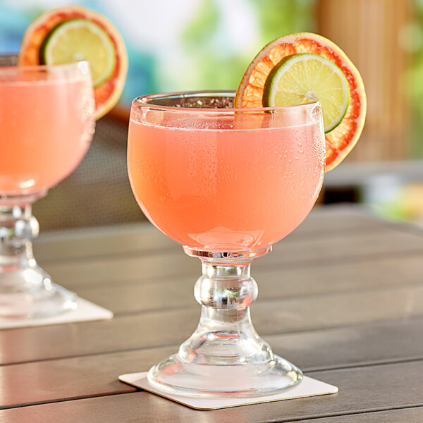 Two Acopa schooner glasses filled with pink drinks and orange slices on a table.