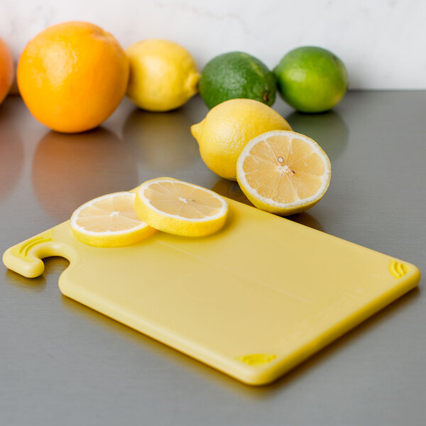 A San Jamar yellow bar size cutting board with sliced lemons on it.