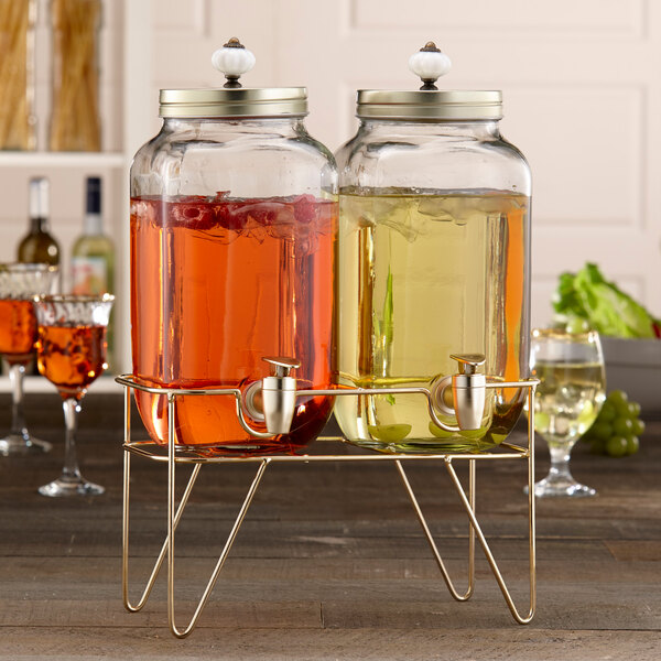 A Stylesetter glass beverage dispenser set on a gold stand with liquid inside.