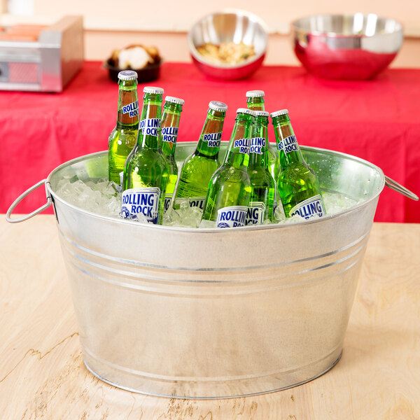 An American Metalcraft galvanized metal tub filled with green beer bottles on a table.