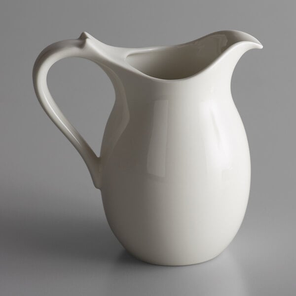 A white RAK Porcelain pitcher with a handle on a gray surface.