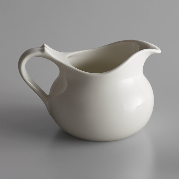 A close-up of a white RAK Porcelain gravy boat with a handle.
