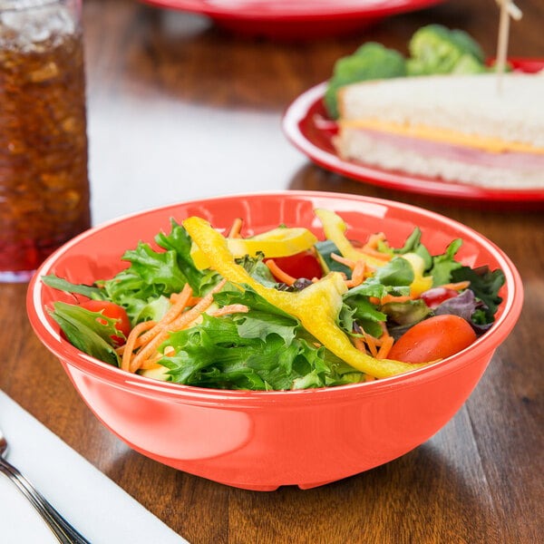 A bowl of salad with vegetables and a sandwich on a table.