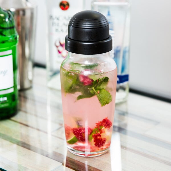 A Libbey glass jar filled with a pink cocktail with fruit and mint leaves next to a Libbey Cobbler Cocktail Shaker.