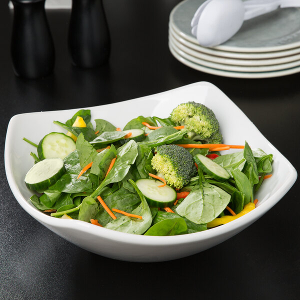 A white square stoneware bowl filled with salad and vegetables.