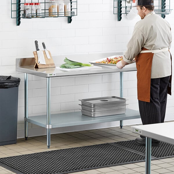A man in a chef's uniform using a Regency stainless steel work table with undershelf.