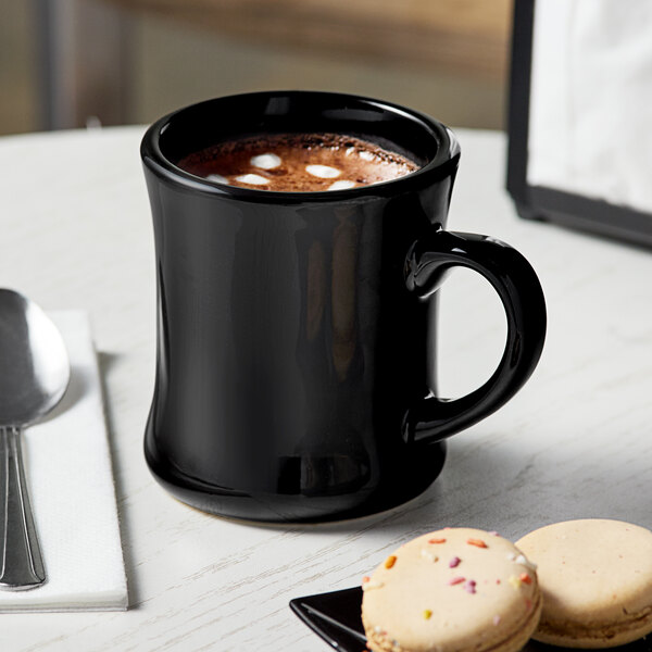 A black Acopa Victor stoneware mug with a drink and cookies on a white table.