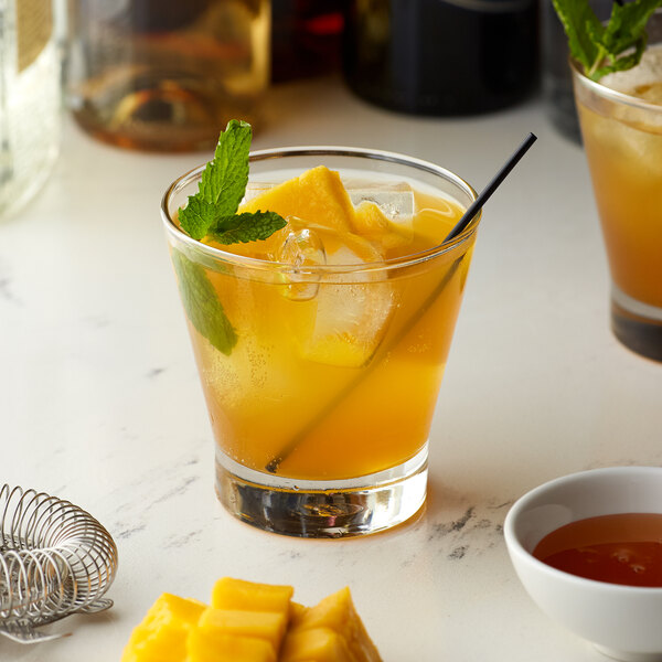 A glass of Monin mango-flavored orange drink with ice and mint leaves.