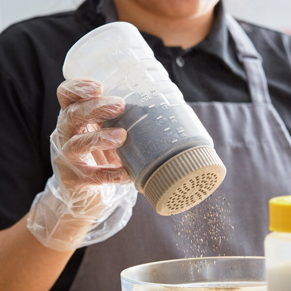 A person in a black apron pouring flour from a Vollrath Polyethylene shaker into a bowl.