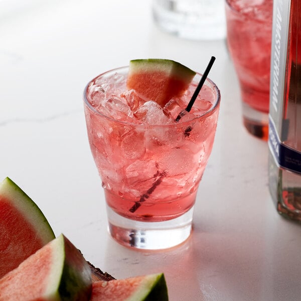 A glass of watermelon flavored drink with a slice of watermelon on the rim.