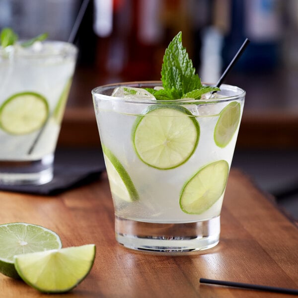 A wooden table with two glasses of limeade with ice, lime slices and mint leaves.