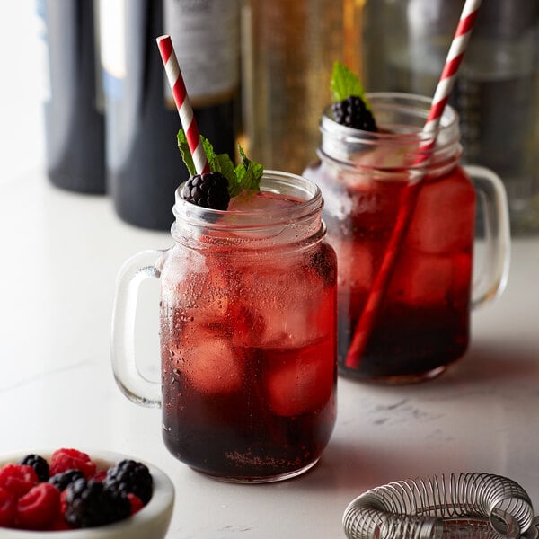 A mason jar filled with a red drink and a straw with a blackberry on it.