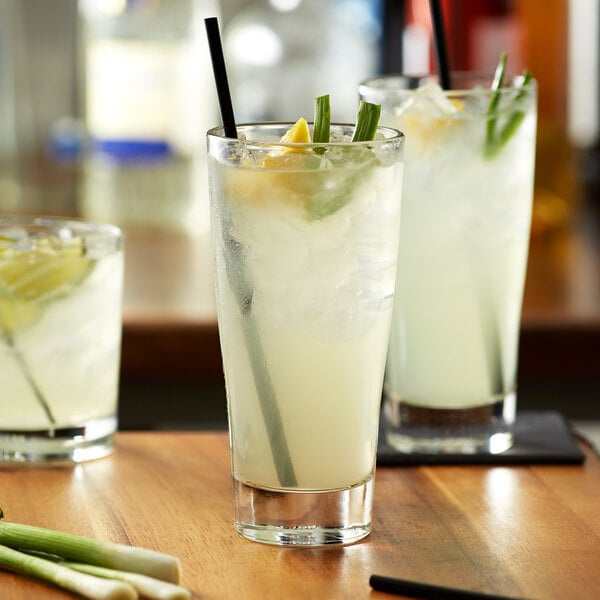 A group of glasses of lemongrass-flavored drinks with straws on a table.