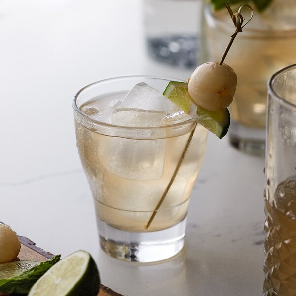 A glass of Monin lychee drink garnished with a lychee on a stick.