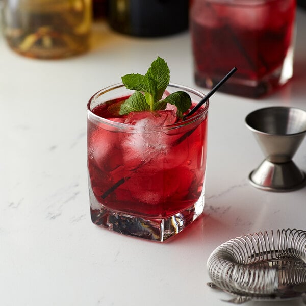 A glass of Monin Sugar Free Pomegranate flavoring syrup with red liquid, ice, and mint leaves with a straw.