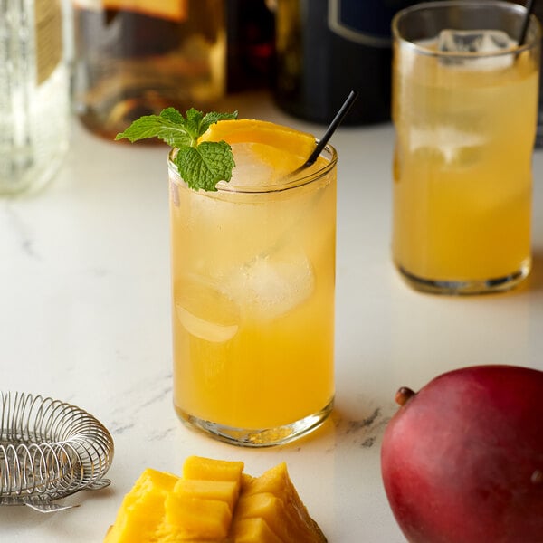 A glass of yellow liquid with a straw and a mango slice on the rim.