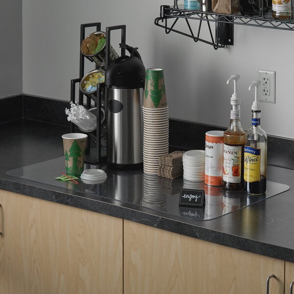 A clear vinyl countertop mat on a kitchen counter with a white and green cup.