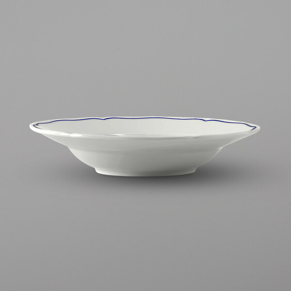 A close up of a Tuxton white china soup bowl with a blue rim.