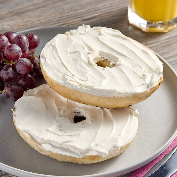 Two bagels with Plain Whipped Cream Cheese Spread on them sit on a plate.
