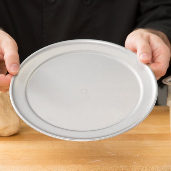 A person holding a round silver pizza pan with dough on it.