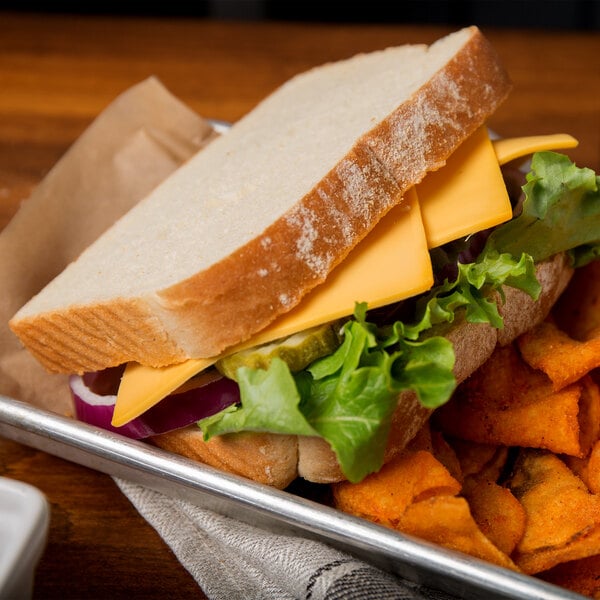 A sandwich with lettuce and Schreiber yellow American cheese on a tray with chips.