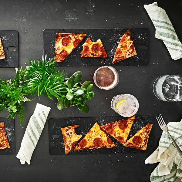 A slate Epicurean bread serving board with slices of pepperoni and cheese pizza on a table with drinks.