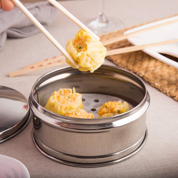 A person using chopsticks to take dumplings out of a stainless steel dim sum steamer.