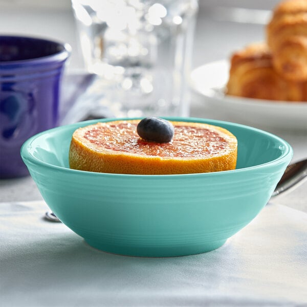 A close-up of a Tuxton blue nappie bowl with a slice of orange and a blueberry on top.