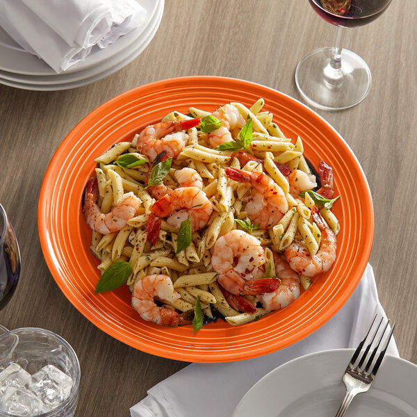 A Tuxton Concentrix papaya china plate with shrimp pasta and basil on it with a fork.