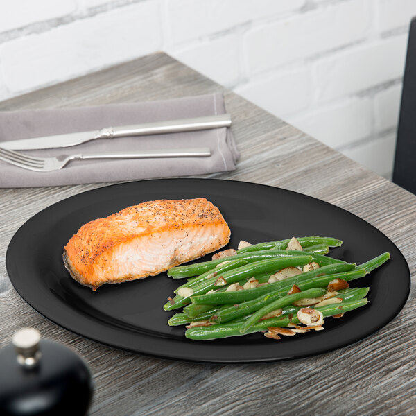 A piece of salmon with green beans on a black oval platter on a table.