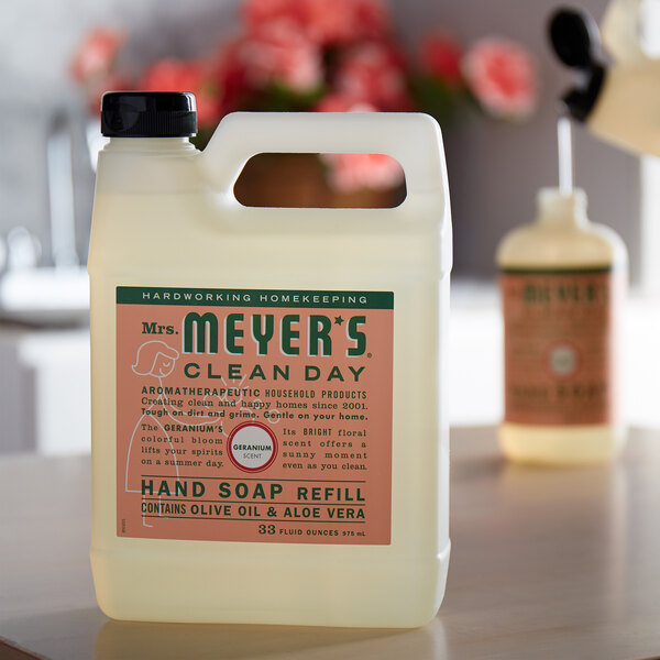 A white plastic container of Mrs. Meyer's Geranium Scented Hand Soap on a table.